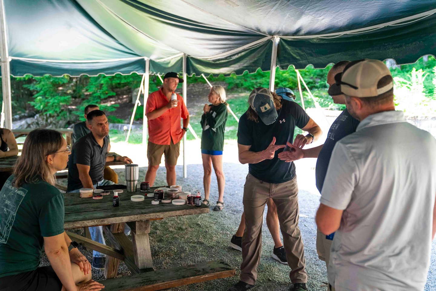 A group of adults listens to a workshop leader under a tent.