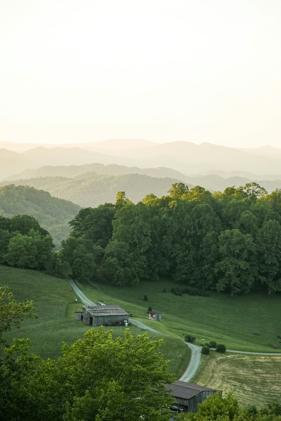 Dirt road leads toward wooden barns among rolling green hills.