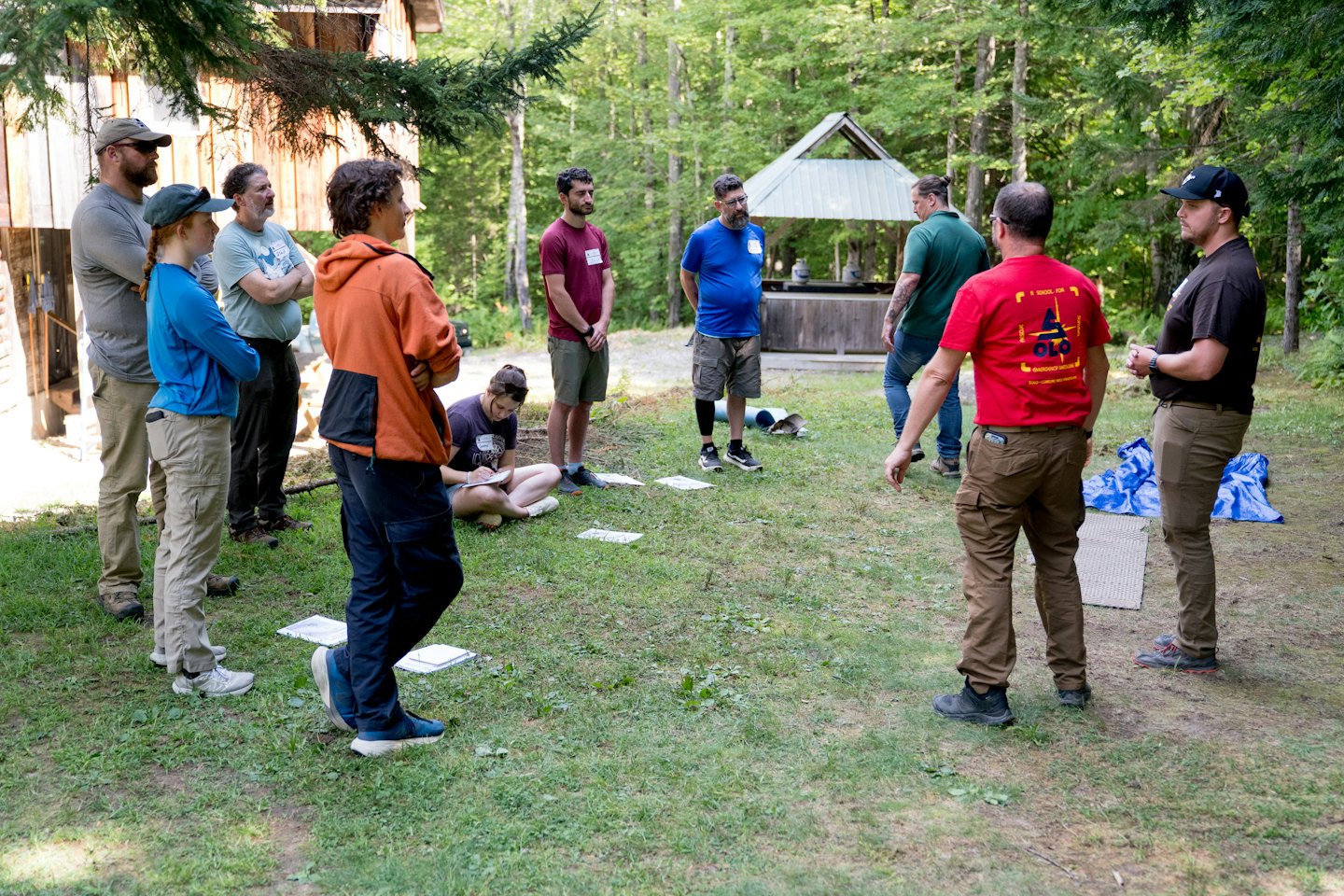 Adults attend an outdoor educational session near a rustic building.